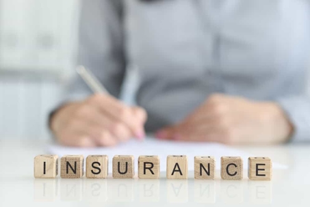 Person writes on a table with the word "insurance" spelled out in block letters