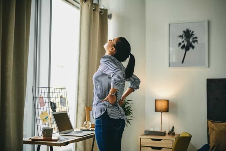 Woman clutches her lower back in pain in her home office