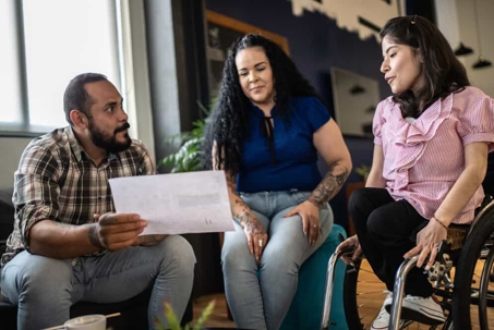 Person in a wheelchair sits with others discussing a document