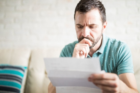 A man sits reading a document, looking concerned.