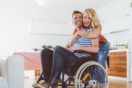 A man in a wheelchair is embraced by a woman.