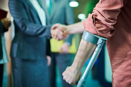 A person with a crutch is shaking hands with someone in a business suit.