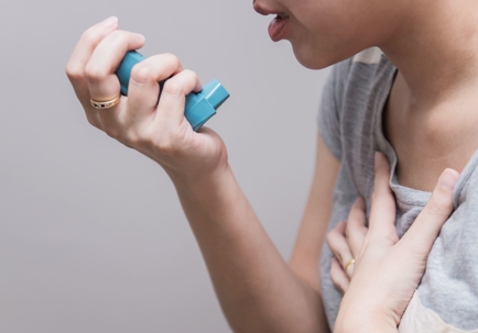 A person is using a blue inhaler, possibly for breathing difficulties.