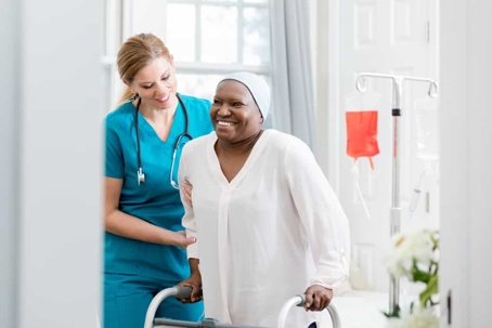 Disabled female patient using a walker gets help walking from a nurse in blue scrubs