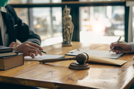 A lawyer and client sit at a desk with a gavel and legal documents