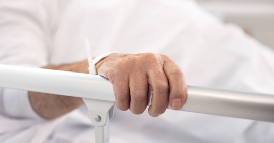 Man suffering from a critical illness holding onto the rail of his hospital bed.