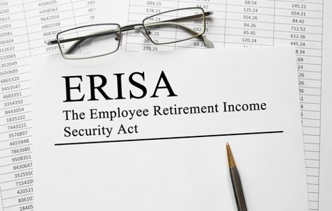 Paper with "ERISA" and "Employee Retirement Income Security Act" printed, glasses, and a pen on top of spreadsheets.