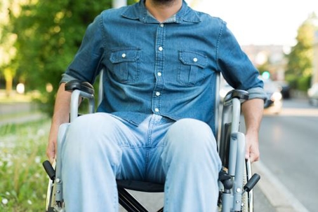 A man in a light blue denim shirt and pants is seated in a light gray wheelchair.
