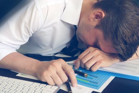 A person in a white shirt is asleep at a desk